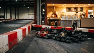 Zwei Karts an einer Indoor-Kartbahn, im Hintergrund die Gastro-Theke mit Pizzaofen